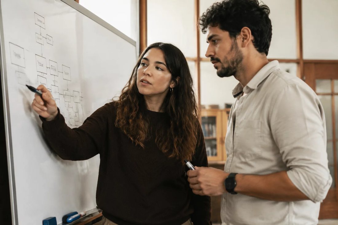 Facilitadora aponta para um mapa de argumento desenhado no quadro branco enquanto um participante acompanha